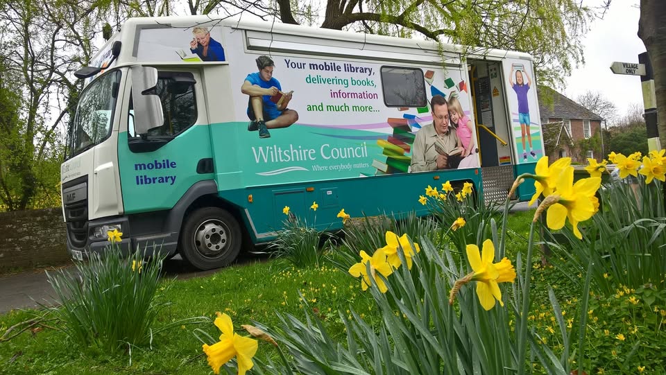 An image of Wiltshire Mobile Library with green grass and daffodils